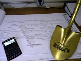 A shovel and calculator resting ontop of some blueprints.